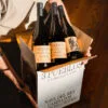 Caja de botellas de vino Albariño 3 Pueblos Rías Baixas sostenida sobre un suelo de madera.