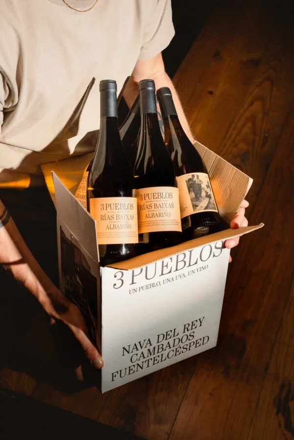Caja de botellas de vino Albariño 3 Pueblos Rías Baixas sostenida sobre un suelo de madera.