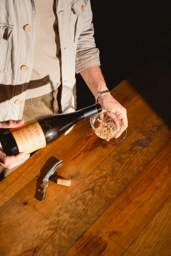 Sirviendo vino blanco 3 Pueblos Rías Baixas Albariño en una copa sobre una mesa de madera.